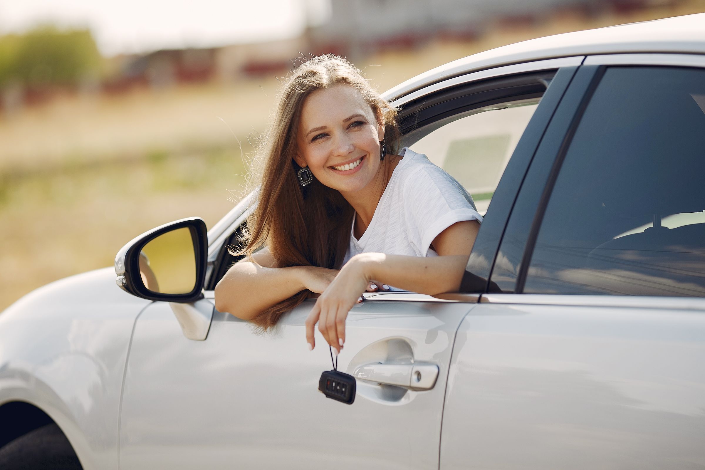 Motorista sorridente apoiada na janela do carro com a chave na mão